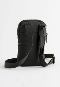 Sac à épaule en tissu noir avec fermeture éclair sur le dessus, bandoulière réglable et corps plat. Présente une texture lisse et un design minimaliste.