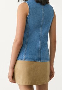 Ärmellose Denim-Weste in Blau mit taillierter Form. Kombiniert mit einem beige Wildleder-Minirock, der eine glatte Textur und einen neutralen Farbkontrast zeigt.