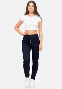 Pantalons bleu marine avec une taille à cordon de serrage, trois boutons et des poches latérales, associés à un crop top blanc et des baskets blanches.