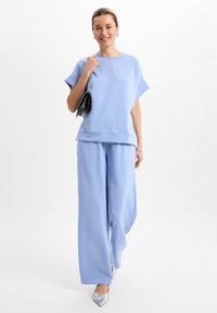 Lichtblauwe top met ruime mouwen en een relaxte pasvorm, gecombineerd met bijpassende brede broek en zilveren puntige schoenen. Inclusief zwarte handtas.