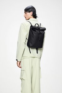 Sort roll-top rygsæk med justerbare stropper, med glat tekstur og minimalistisk design, båret af en person i lyst tøj.