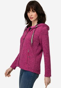 Fuchsia zip-up hoodie med enTexturerad mönster, kontrasterande dragkedjor och två sidofickor. Har en huva och långa ärmar.