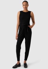 Haut sans manches noir avec un col rond, associé à un pantalon noir taille haute et fuselé, doté d'une ceinture en tissu nouée et de poches latérales.