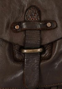 Primo piano di una borsa in pelle marrone con una superficie testurizzata, componenti metallici, una patta cucita e una tracolla in pelle con chiusura a bottone.