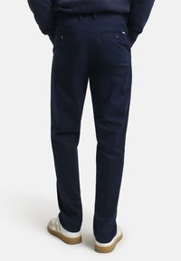 Helleblau Baumwollchinos mit geradem Bein, Seitentaschen und zwei Gesäßtaschen mit Knopfverschluss. Kombiniert mit weißen Sneakern.