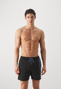 Costume da bagno neri con un laccetto viola a contrasto e dettagli nei pannelli laterali. Realizzati in tessuto leggero, presentano una vita elasticizzata.