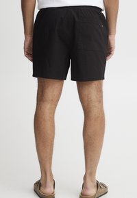 Fekete pamut sort, rugalmas derékkal, hátsó zsebbel és laza szabással. Világos barna slip-on szandállal viselve.