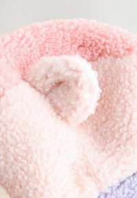 Round plush textile in pink and light pink hues featuring a soft, fluffy texture, with a curl accent visible on the surface.