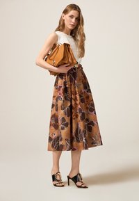 Gonna floreale marrone con design a campana, abbinata a una blusa senza maniche bianca e sandali neri con tacco. Presenta una borsa marrone chiaro con tracolla a catena.
