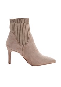 Stivale alla caviglia beige in suede con punta a punta e parte superiore in maglia a coste simile a un calzino, dotato di un sottile tacco di media altezza su uno sfondo bianco.