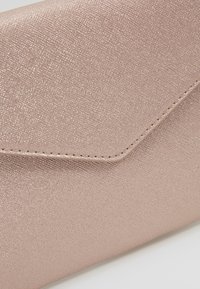 Kopertówka w kolorze różowego złota wykonana z teksturowanego materiału, z charakterystyczną, spiczastą klapką, przeszywanymi krawędziami i metalicznym połyskiem.