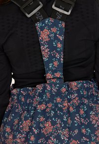 Blommönstrade hängslen har en mörkblå bakgrund med rosa och teal blommor. Tyget är mjukt och har en flädrad midjebandsdesign.