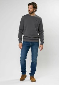 Grijze sweatshirt met geribde manchetten en onderrand, gecombineerd met blauwe jeans en bruine schoenen. De sweatshirt heeft een klein logo op de borst.