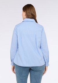 Camisa de botones azul claro con rayas verticales blancas, de mangas largas y cuello puntiagudo. Tela suave con un corte relajado.