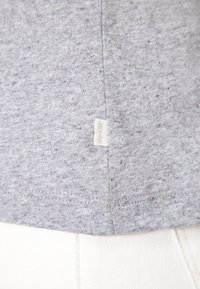 Tessuto di maglietta in cotone grigio con una sottile texture maculata, con un piccolo etichetta bianca sul margine. L'orlo è rifinito in modo ordinato.