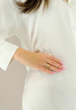 Camicia di seta bianca con una vestibilità ampia. La mano presenta un anello d'oro con un design ondulato e unghie lunghe e curate di colore rosa.