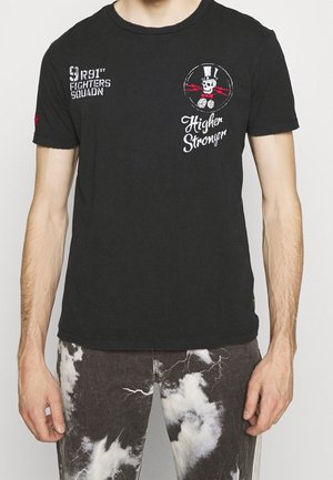 Sort T-shirt med hvid tekst "9 R81st Fighters Squadn," kranie iført høj hat og butterfly med terninger, og ordene "Higher Stronger" på brystet.