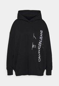 Felpa con cappuccio nera realizzata in tessuto morbido, con una tasca frontale e testo grafico. Grande logo 'CALVIN KLEIN JEANS' in stampa bianca e argento.