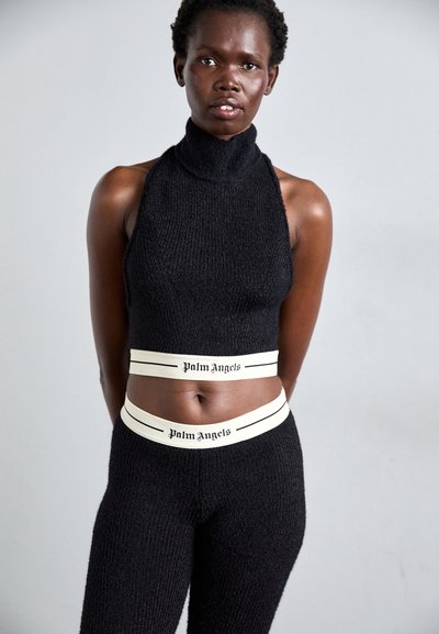 Black knit crop top with a high collar and fitted design, paired with matching high-waisted leggings featuring cream-colored branded waistbands.