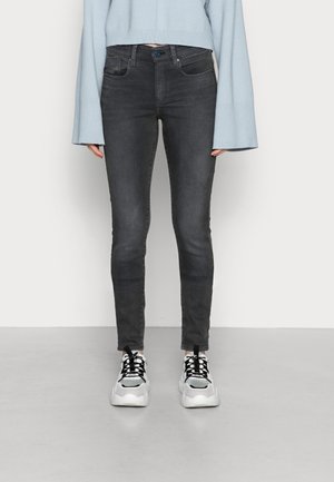 Jeans ajustados en denim negro lavado con un diseño clásico de 5 bolsillos. Combinados con un suéter cortito azul claro y zapatillas blancas.