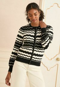 Czarny i biały kardigan w wzór w zygzaki, okrągły dekolt, zapięcie na guziki, ribbowane mankiety i teksturowany materiał.