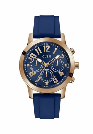 Montre Round Guess avec un bracelet en silicone bleu marine. Boîtier doré, grands chiffres arabes dorés, et trois sous-cadrans sur un cadran bleu.