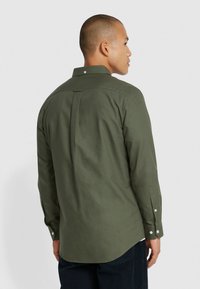 Maglietta a maniche lunghe verde oliva con polsini abbottonati, colletto classico e dettaglio a piega sul retro. Tessuto di cotone morbido, orlo curvo.