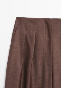 Brązowe spodnie materiałowe z plisami, posiadające teksturowany splot, gładki przód oraz boczną kieszeń, o dopasowanym kroju i czystych liniach.