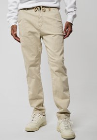 Pantaloni beige realizzati in un tessuto morbido, dotati di una vita elastica con cordino, design a gamba dritta e tasche laterali.