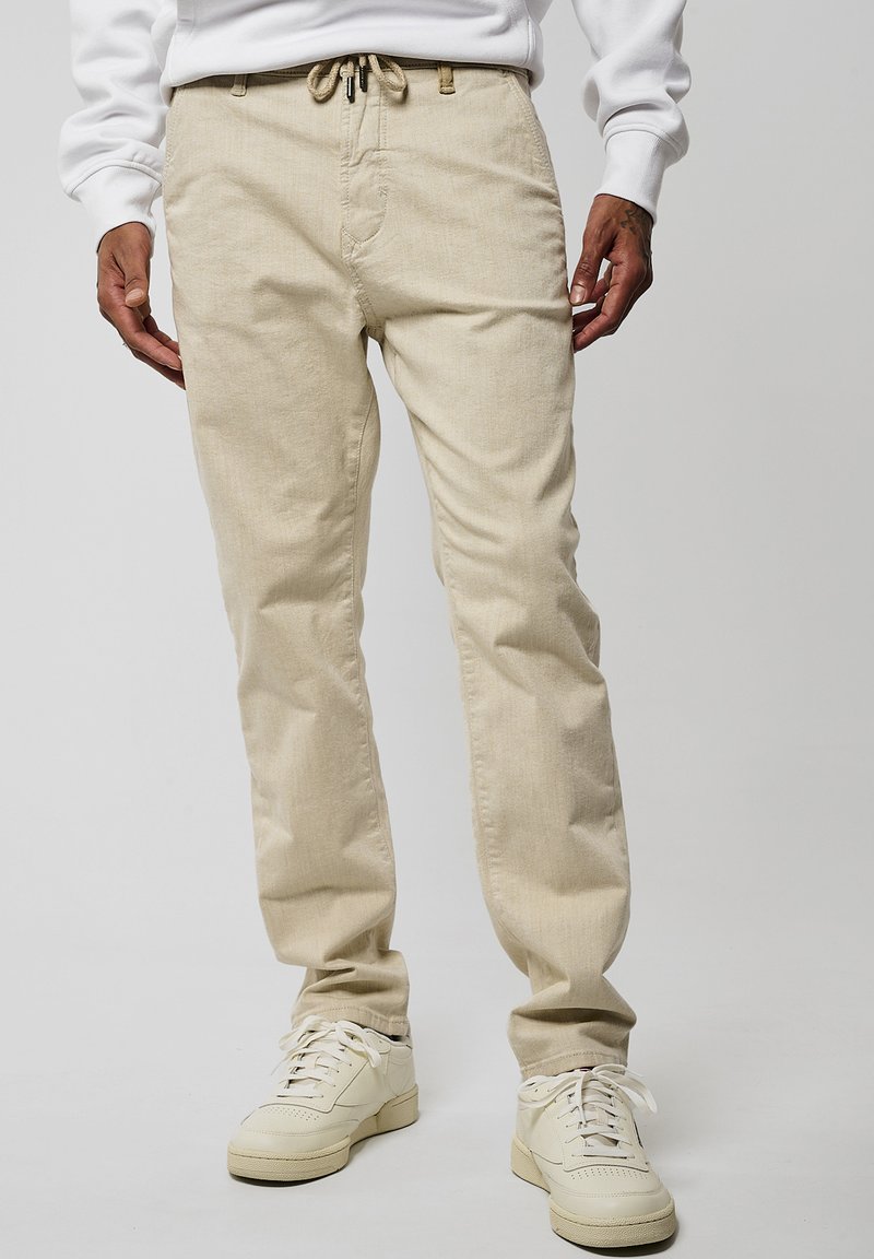 Pantaloni beige realizzati in un tessuto morbido, dotati di una vita elastica con cordino, design a gamba dritta e tasche laterali.