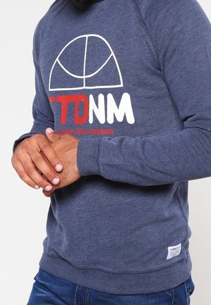 Sudadera azul marino con cuello redondo, que presenta un estampado gráfico en blanco y rojo. Puños y dobladillo acanalados con una pequeña etiqueta en el lado inferior.