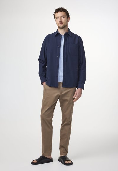 Navy button-up shirt over a light blue polo, paired with tan pants and black slide sandals. Smooth textures and classic cut throughout.