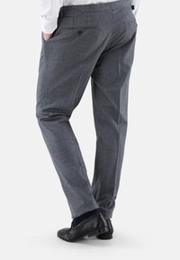 Graue Wollhose mit strukturierter Oberfläche, ausgestattet mit einem flachen Bund, seitlichen Taschen und einer taillierten Passform. Getragen mit schwarzen Slippern.