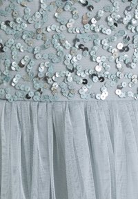 Robe bleu clair avec un corsage pailleté orné de sequins ronds et une jupe en tulle doux, créant un effet texturé et superposé.