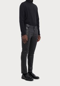 Černé rolákové tričko, doplněné o úzké černé kožené kalhoty s předním zipem a kapsami. Celý outfit doplňují černé loafers.