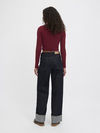 Langermet burgunder topp parret med mørkeblå høyhalsede jeans med oppbrettede sømmer og synlig lysbrun stikking.