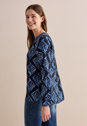 Blusa a maniche lunghe di colore blu navy con un motivo geometrico in tonalità di blu. Tessuto morbido, vestibilità ampia e design con scollo rotondo.