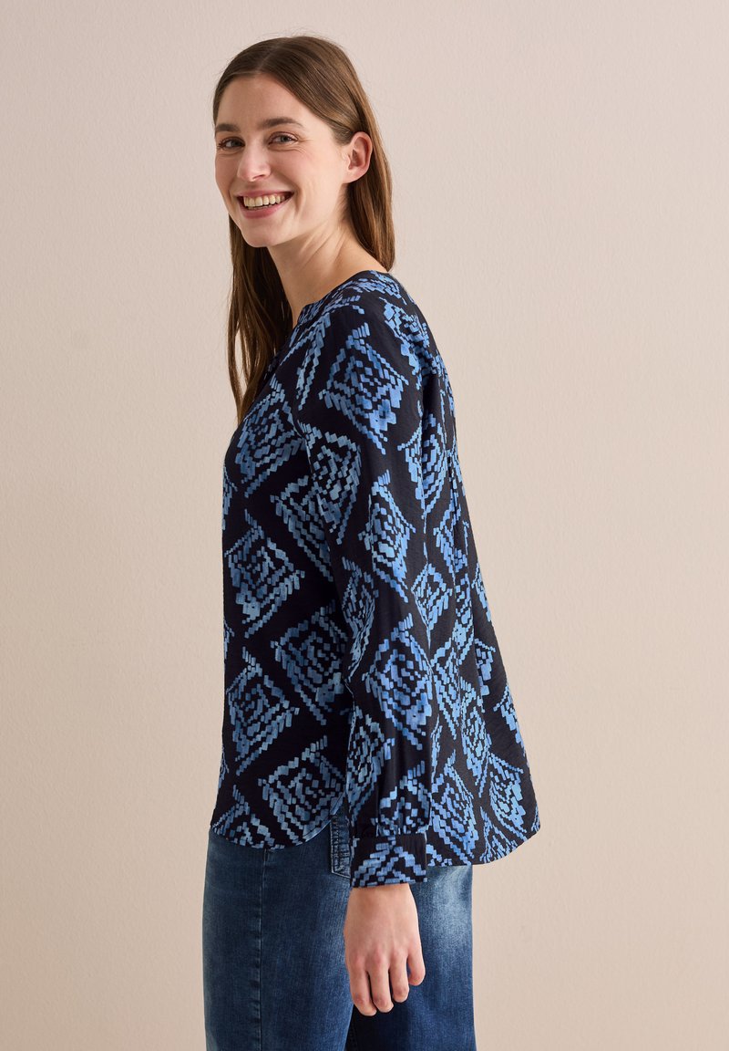 Blusa a maniche lunghe di colore blu navy con un motivo geometrico in tonalità di blu. Tessuto morbido, vestibilità ampia e design con scollo rotondo.
