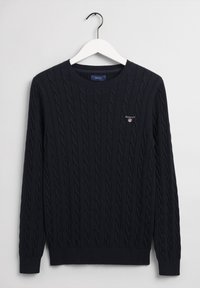 Pull bleu marine à col rond en maille torsadée avec logo GANT brodé sur la poitrine, présenté sur un cintre blanc sur un fond clair.