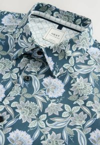 Blumenmusterhemd aus dunkelblauem Stoff mit hellblauen und grünen Motiven. Verfügt über einen spitzen Kragen, eine Knopfleiste und ein schlankes Design.