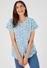 Camisa de botón con base azul claro, con un patrón floral en verde y azul oscuro. Mangas cortas y dobladillo redondeado.