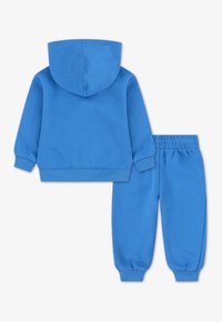Haut à capuche bleu avec une capuche attachée et un pantalon de jogging assorti. Les deux pièces sont en tissu doux, avec des poignets et une taille élastiques.