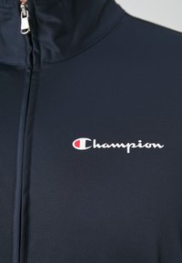 Giacca navy con zip a quarti realizzata in tessuto morbido, con il logo Champion bianco sul lato sinistro del petto e colletto con zip.