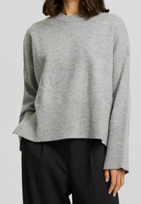 Szary sweter z dzianiny z prążkowanym dołem i mankietami, o luźnym kroju i okrągłym dekolcie, wykonany z miękkiego, teksturowanego materiału.