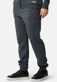 Grå, elastiska joggers i bomullsmix med sidfickor och avsmalnande muddar, i kombination med svarta sneakers med slät yta och vita sulor.