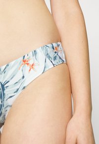 Parte de baixo de biquíni com uma base azul clara, apresentando padrões de folhas tropicais e flores em verde e laranja, feita de um tecido suave e elástico.