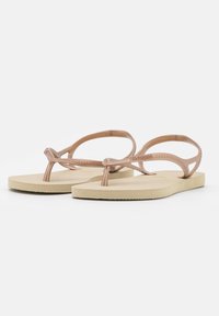 Infradito in gomma beige con una suola testurizzata, caratterizzate da un design con cinturino aperto sottile e un logo discreto sulla parte superiore del cinturino.