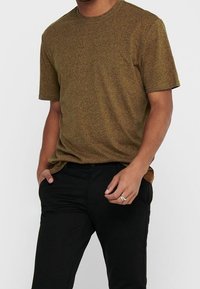 Olivgrön texturerad bomullströja med rund hals och korta ärmar, kombinerad med svarta byxor. Figursydd design med en slät finish.