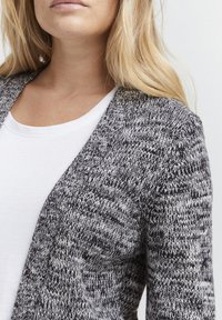 Pletený cardigan v černobílé, s vzorem ve tvaru cik-cak, otevřeným designem a měkkou strukturou. Noste přes bílou košili.