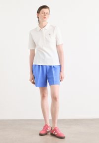 Vit pikétröja med korta ärmar och knäppning, blå shorts med avslappnad passform och rosa sneakers med klassisk design.